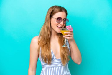 Mavi arka planda mayo giymiş ve elinde kokteyl tutan genç bir kadın.