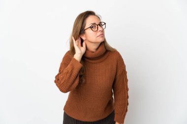 Orta yaşlı Brezilyalı bir kadın beyaz arka planda izole edilmiş bir şekilde elini kulağına koyarak bir şeyler dinliyor.