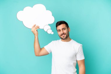 Genç, yakışıklı, beyaz bir adam mavi arka planda izole edilmiş. Elinde bir konuşma balonu var.