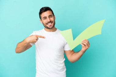 Mavi arka planda izole edilmiş yakışıklı beyaz bir adam elinde bir çek simgesi tutuyor ve ona doğrultuyor.