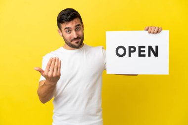 Sarı arka planda izole edilmiş yakışıklı beyaz bir adam. Elinde açık yazılı bir levha var.