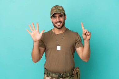 Mavi arka planda izole edilmiş künyeli asker. Parmakları olan altı kişi saydım.