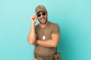 Mavi arka planda izole edilmiş, gözlüklü ve mutlu bir asker.