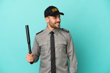 Mavi arka planda izole edilmiş genç bir güvenlik görevlisi yana bakıyor ve gülümsüyor.