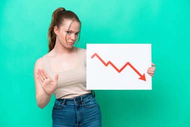 Yeşil arka planda izole edilmiş beyaz bir kadın elinde azalan bir istatistik ok sembolü olan bir tabela tutuyor ve dur işareti yapıyor.