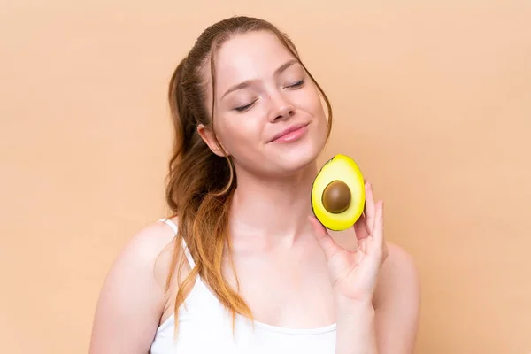 Junges Kaukasisches Mädchen Isoliert Auf Beigem Hintergrund Mit Einer Avocado — Stockfoto