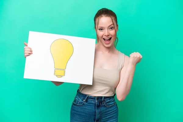 Young Caucasian Woman Isolated Green Background Holding Placard Bulb Icon — Stock Photo, Image