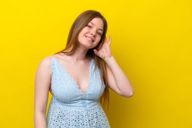 Sarı arka planda izole edilmiş genç beyaz bir kadın. Kulağına elini sürerek bir şeyler dinliyor.