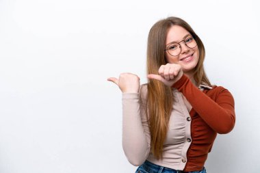 Beyaz arka planda izole edilmiş genç beyaz kadın bir ürünü sunmak için kenarı işaret ediyor.