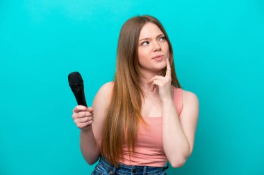 Kafkasyalı şarkıcı, mavi arka planda izole edilmiş bir mikrofonu kaldırıyor.