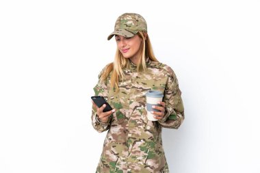 Beyaz arka planda izole edilmiş askeri bir kadın elinde kahve ve bir cep telefonu tutuyor.