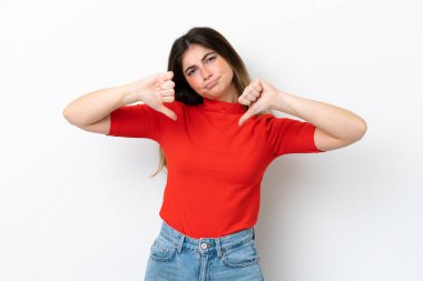 Beyaz arka planda izole edilmiş genç beyaz kadın baş parmağını iki eliyle aşağı gösteriyor.