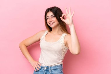 Pembe arka planda izole edilmiş beyaz bir kadın parmaklarıyla tamam işareti gösteriyor.