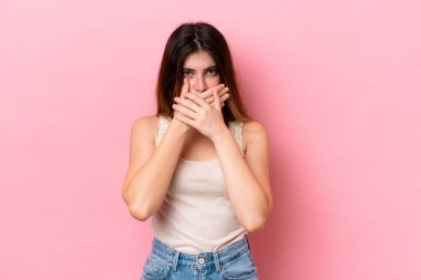 Pembe arka planda izole edilmiş genç beyaz kadın elleriyle ağzını kapatıyor.