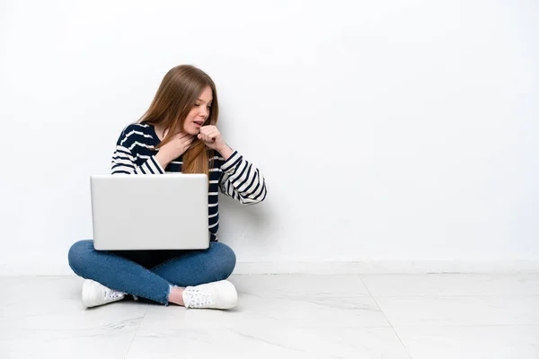 Young caucasian woman with a laptop sitting on the floor isolated on white background is suffering with cough and feeling bad