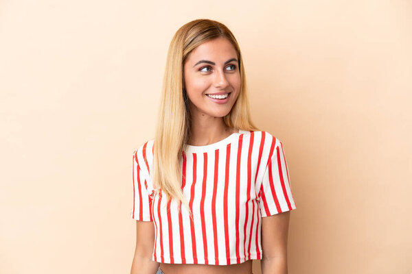 Blonde Uruguayan girl isolated on beige background looking to the side and smiling