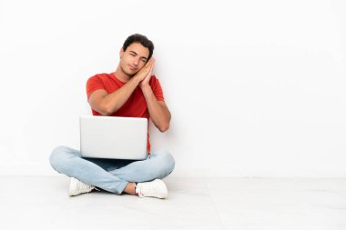 Caucasian handsome man with a laptop sitting on the floor making sleep gesture in dorable expression