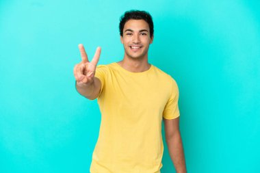 Izole mavi arka plan üzerinde Kafkas yakışıklı adam gülümseyerek ve zafer işareti gösteren