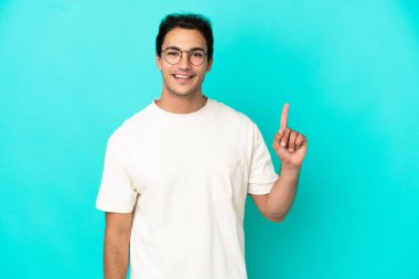 Izole mavi arka plan üzerinde Kafkas yakışıklı adam gösteren ve en iyi işareti bir parmak kaldırma