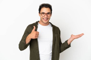 Caucasian handsome man over isolated white background holding copyspace imaginary on the palm to insert an ad and with thumbs up