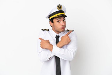 Airplane pilot over isolated white background pointing to the laterals having doubts