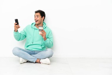 Kafkasyalı yakışıklı bir adam kahve alıp götürmek için yerde oturuyor ve bir de cep telefonu.