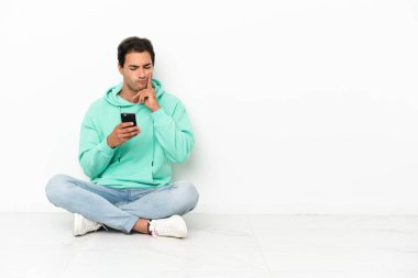 Caucasian handsome man sitting on the floor thinking and sending a message