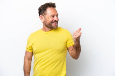 Beyaz arka planda izole edilmiş orta yaşlı beyaz bir adam bir ürün sunmak için kenarı işaret ediyor.