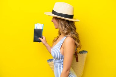 Genç bir kadın, mutlu bir ifadeyle sarı arka planda izole bir şekilde plaja tatile gider.