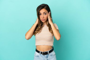 İzole edilmiş mavi arka planı olan genç bir kadın hayal kırıklığına uğramış ve kulaklarını kapatmış.