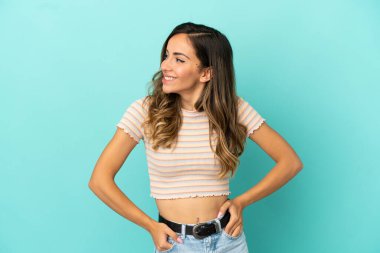 Soyutlanmış mavi arka planda genç bir kadın yana bakıyor ve gülümsüyor.