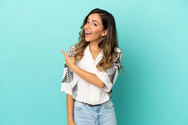 İzole edilmiş mavi arka planı olan genç bir kadın şaşırmış ve işaret ediyor.