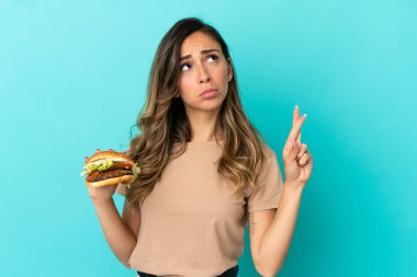 İzole edilmiş arka planda hamburgerini tutan genç bir kadın şans diliyor.