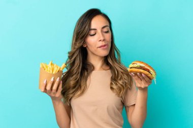 Arkaplanda kızarmış cips ve hamburger tutan genç bir kadın.