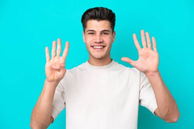 Genç beyaz adam mavi bakkalda izole edilmiş. Parmaklarıyla dokuz kişi sayıyor.