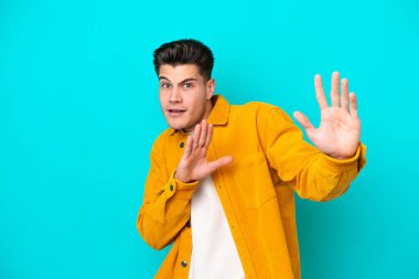 Genç, yakışıklı, beyaz bir adam, mavi bakkalda izole edilmiş, gergin, ellerini öne uzatıyor.