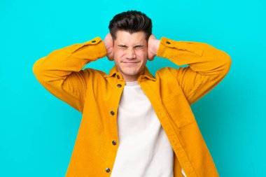 Genç, yakışıklı, beyaz bir adam mavi fırında izole edilmiş hayal kırıklığına uğramış ve kulaklarını kapatmış.