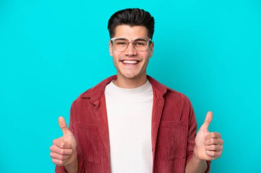 Genç, yakışıklı, beyaz bir adam mavi fırında tek başına, gözlüklü ve başparmağı havada.