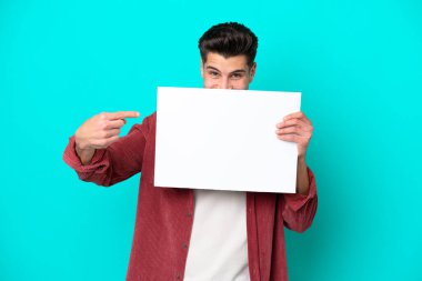 Genç, beyaz bir adam mavi bir bakkalda izole edilmiş boş bir levha tutuyor ve arkasında saklanıyor.