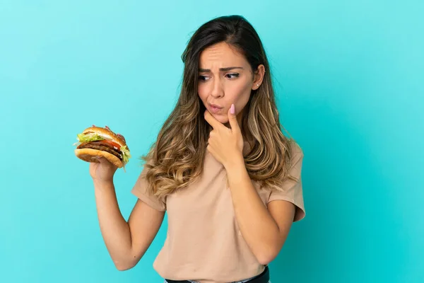 Young Woman Holding Burger Isolated Background Having Doubts Thinking — Stock Photo, Image