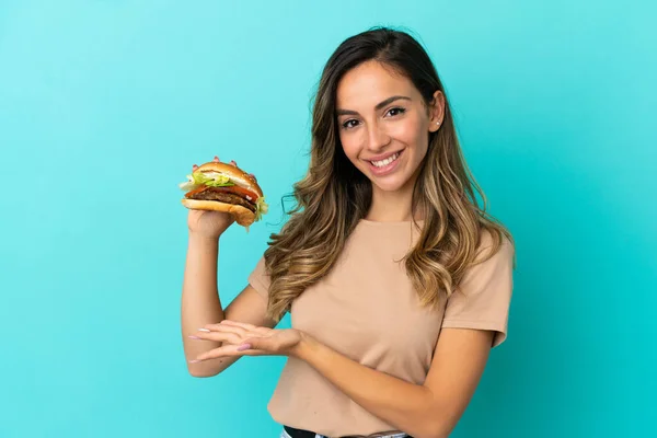 Young Woman Holding Burger Isolated Background Extending Hands Side Inviting — Zdjęcie stockowe