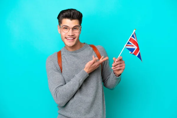 Young caucasian man holding an United Kingdom flag isolated on blue background extending hands to the side for inviting to come