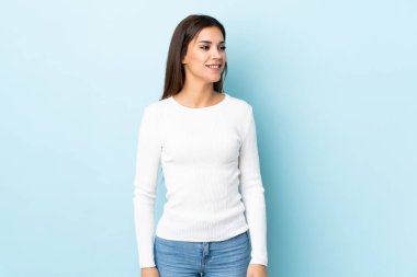 Mavi arka planda soyutlanmış genç beyaz kadın yana bakıyor ve gülümsüyor.