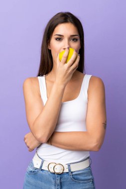 Mor arka planda izole edilmiş, elma yiyen beyaz bir kadın.