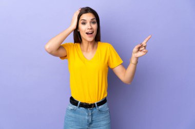 İzole edilmiş arka planda yaşayan beyaz bir kadın şaşırmış ve parmağıyla kenarı işaret ediyor.