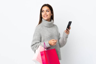 Beyaz arka planda izole edilmiş beyaz bir kadın elinde alışveriş çantaları ve cep telefonu tutuyor.