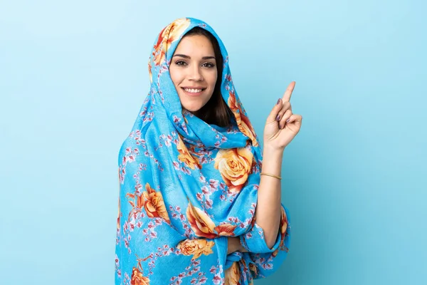 Young Moroccan woman with traditional costume isolated on blue background showing and lifting a finger in sign of the best