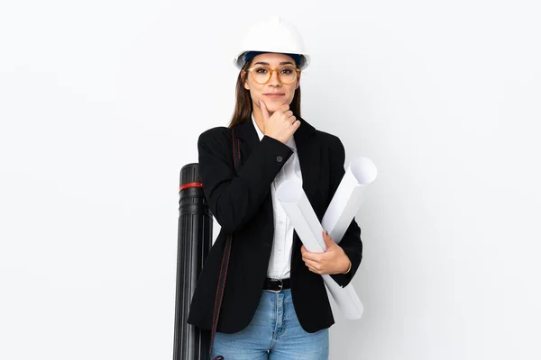 Young architect caucasian woman with helmet and holding blueprints over isolated background laughing