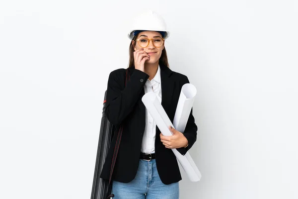 Young architect caucasian woman with helmet and holding blueprints over isolated background nervous and scared