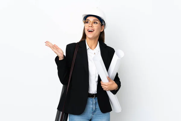 Young architect caucasian woman with helmet and holding blueprints over isolated background with surprise facial expression